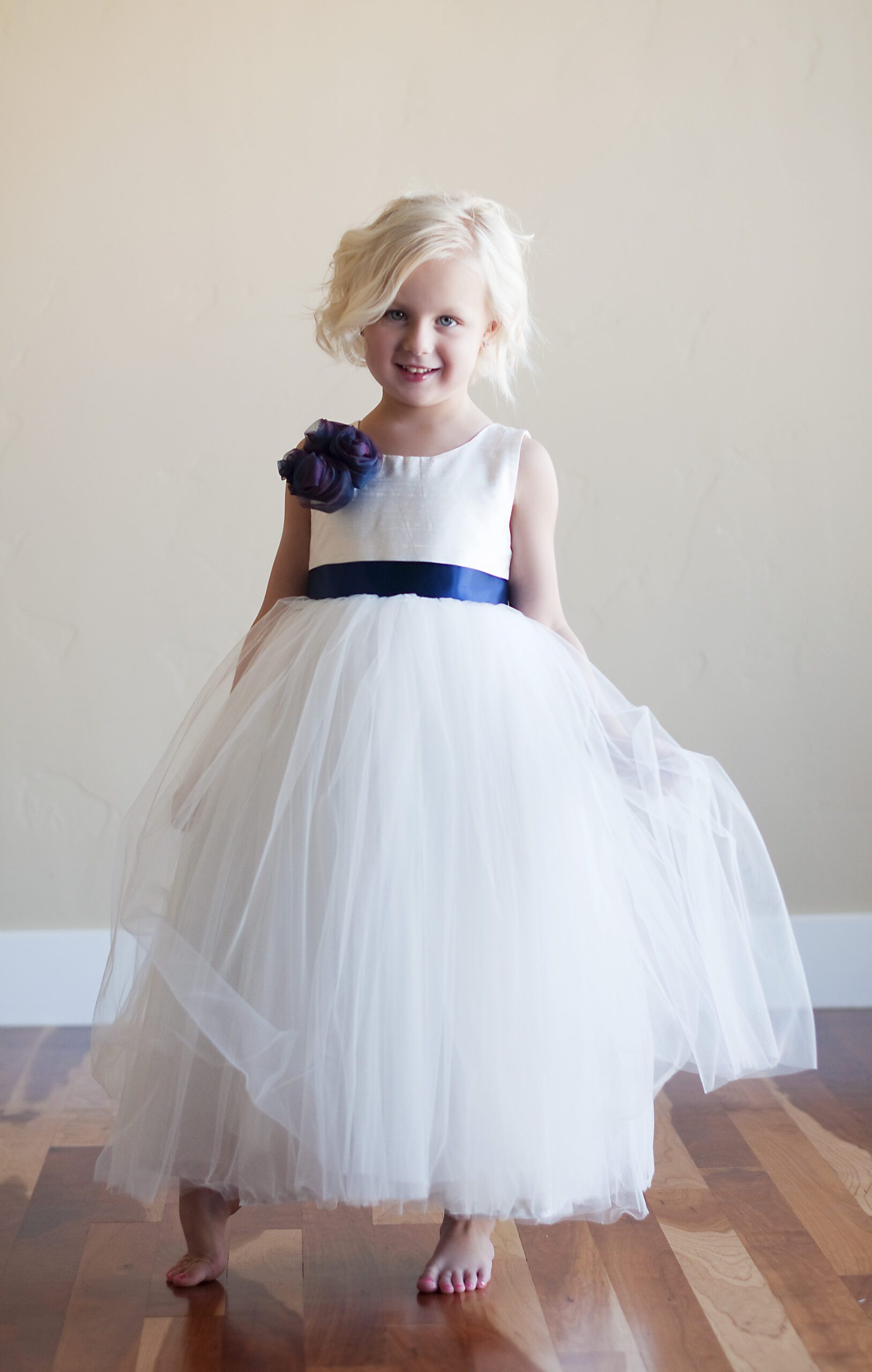 A photo of a 5 year old flower girl wearing a flower girl dress in silk and tulle with a blue flower on the shoulder