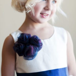 A photo of a flower girl wearing an ivory dress with a blue organza flower and full tulle skirt