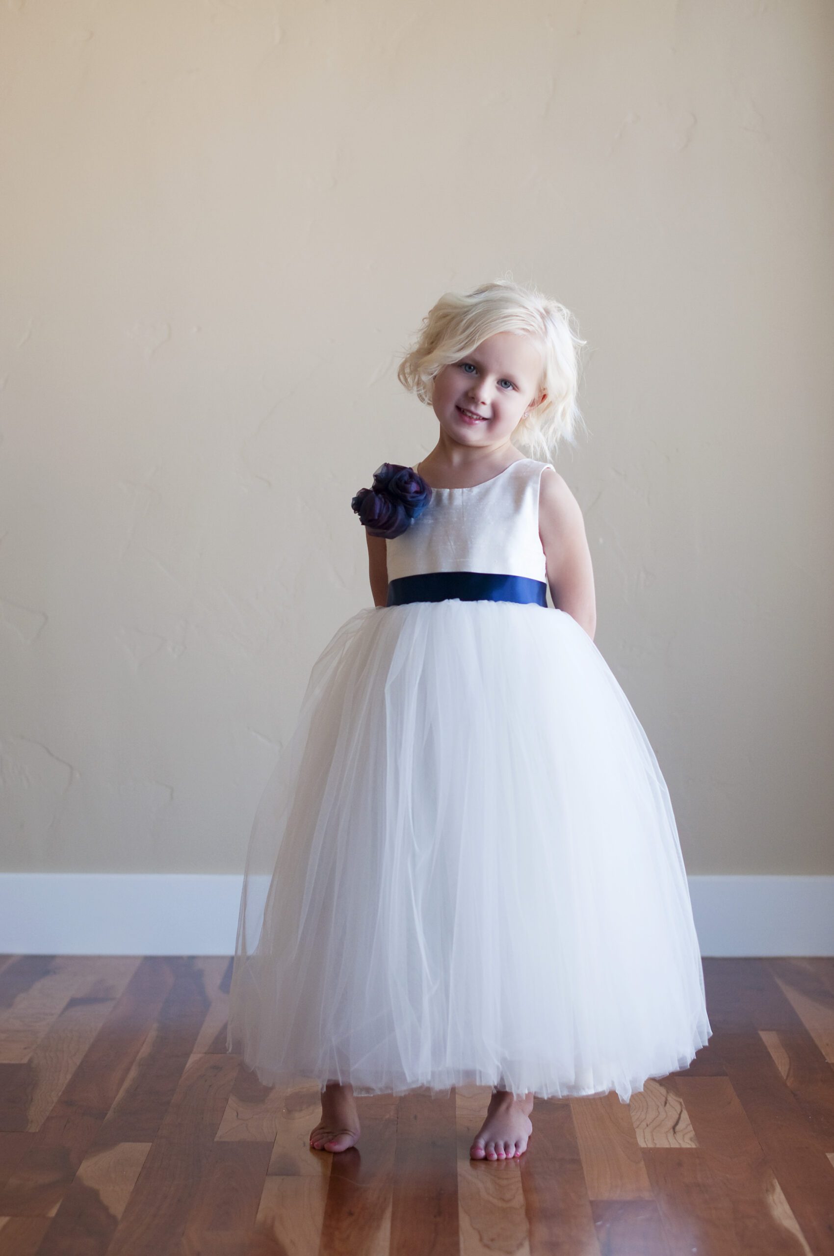 A photo of a 5 year old flower girl wearing a flower girl dress in silk and tulle with a blue flower on the shoulder. The dress is available in ivory and white
