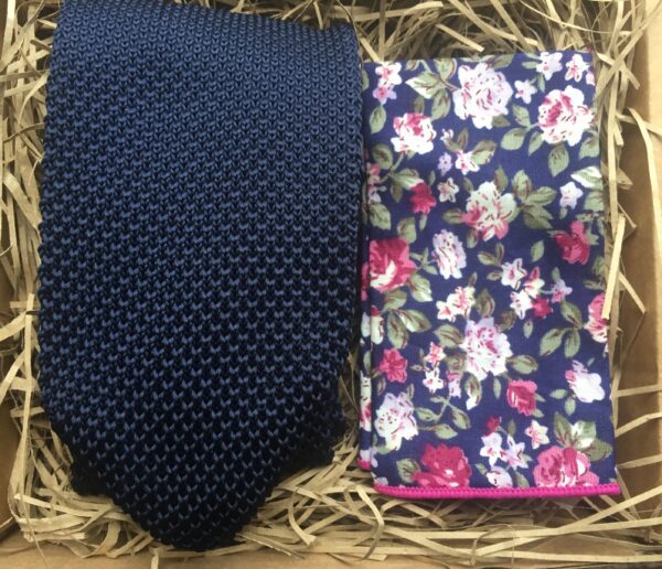 A photo of a navy blue knitted mens tie with a blue floral pocket square