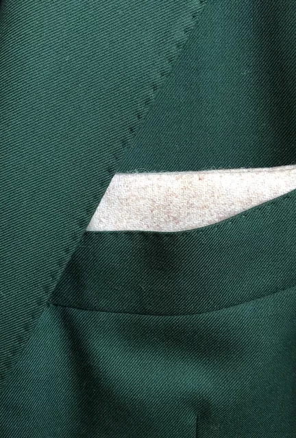 A photo fo a cream wool pocket square in the breast pocket of a green suit