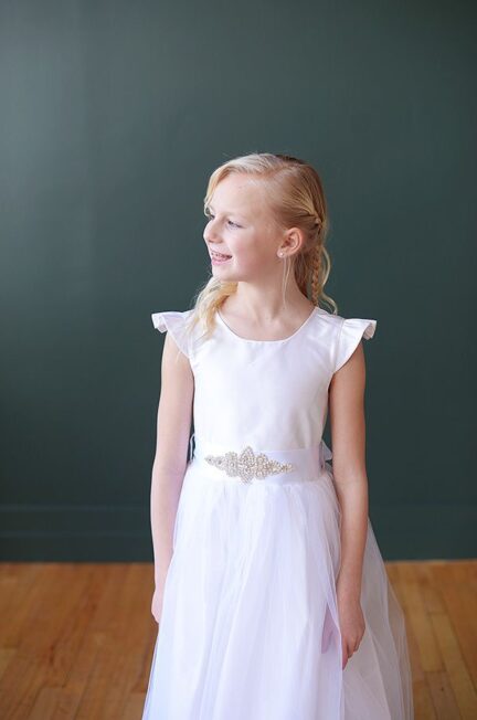 A photo of an 8 year old girl wearing a silk first communion dress in white with aa tulle skirt and diamante motif