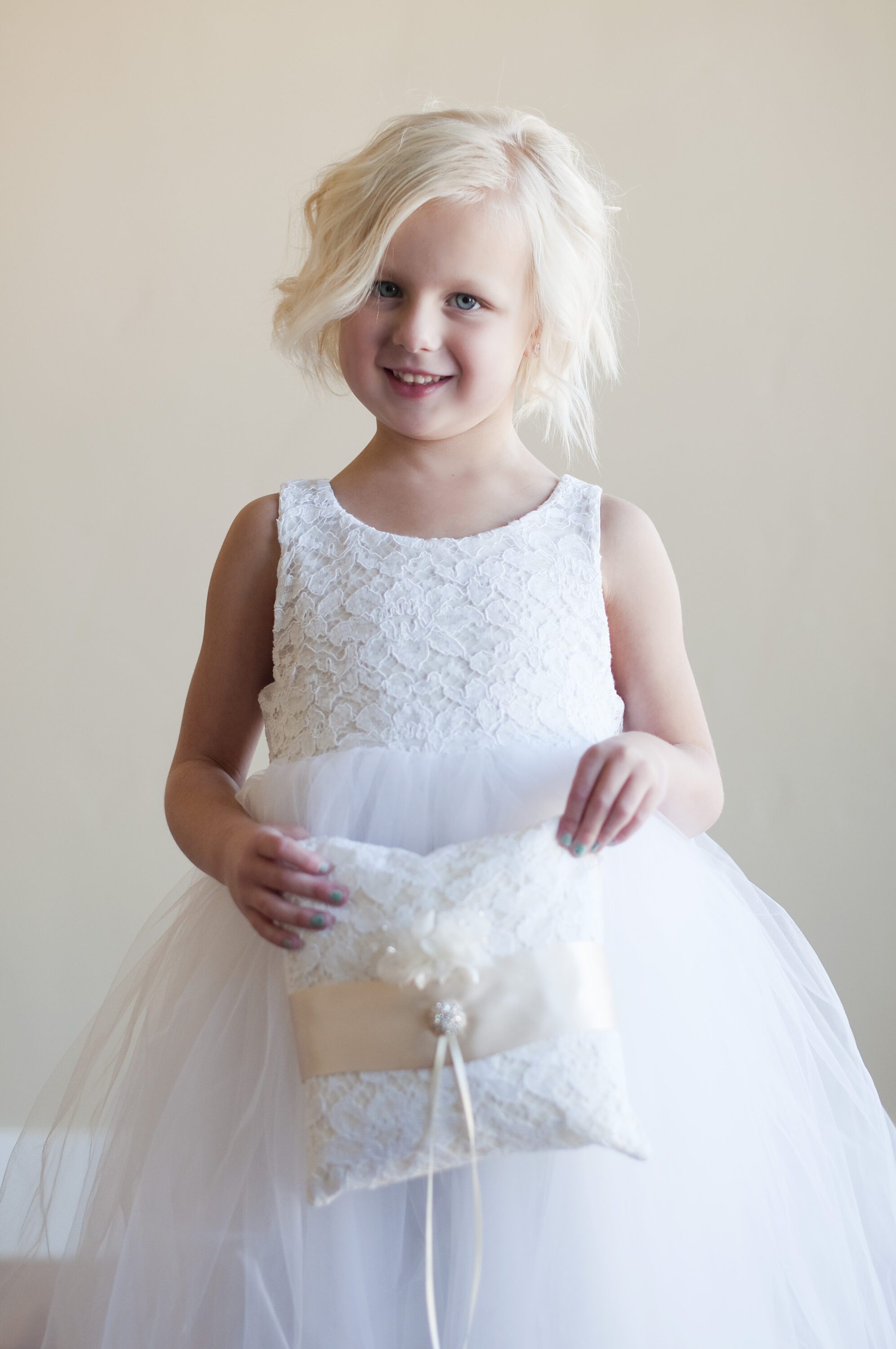 A young flower girl wearing an ivory and white lace flower girl dress