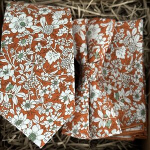 A photo of an orange floral tie, bow tie and pocket square set