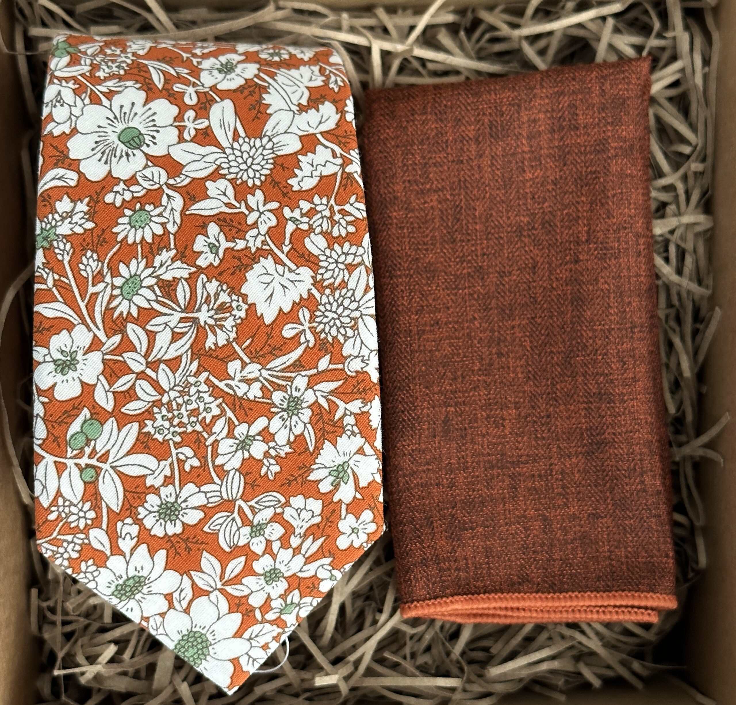 A photo of an orange floral tie and burnt orange pocket square