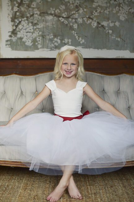 A photo of a flower girl wearing a full tulle skirt with a red sash and oversized bow
