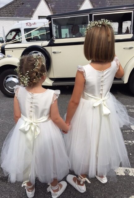 A photo of two flower girls wearing ivory and silk dresses with a sash
