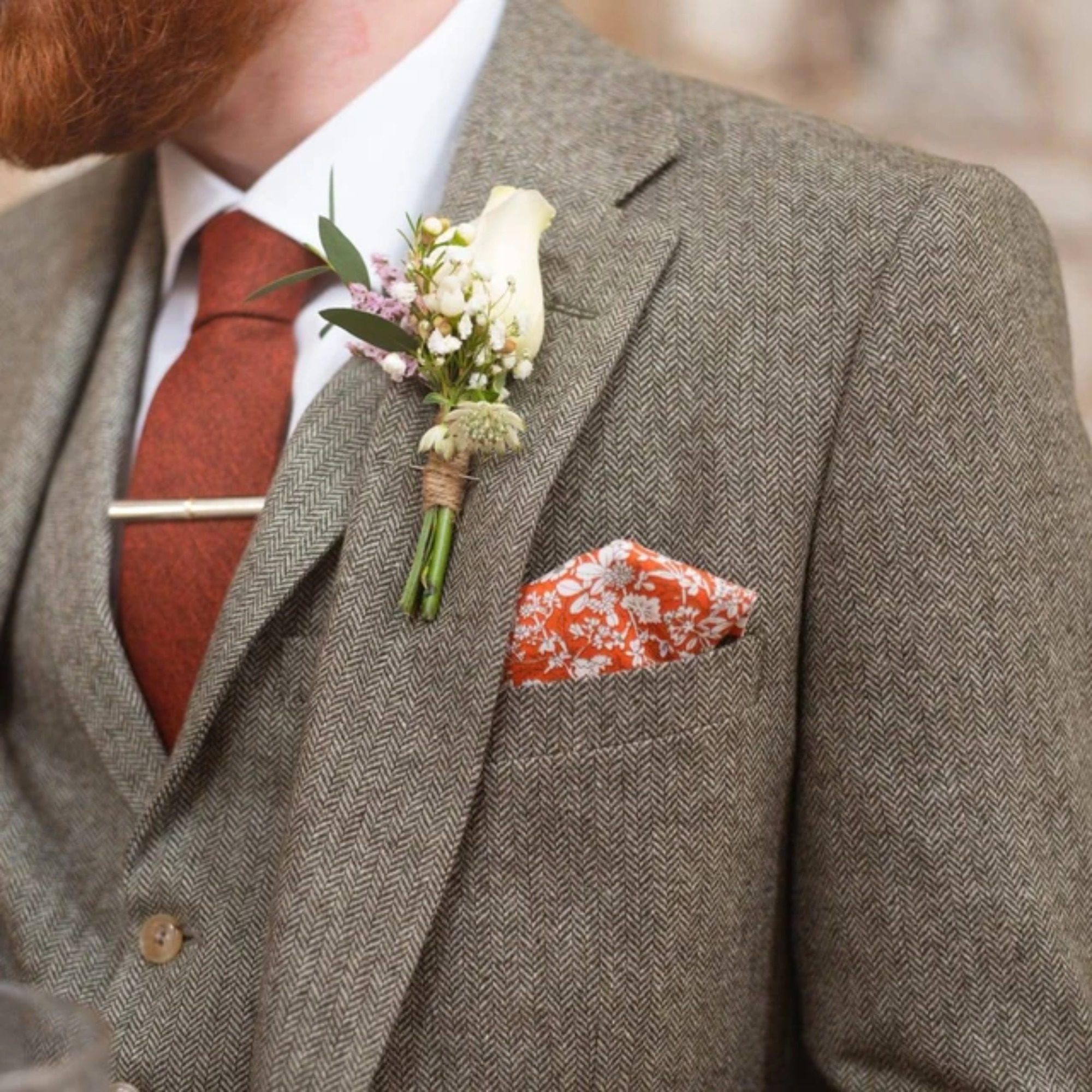 A photo of a groom wearing burnt orange tie and an orange floral pocket square