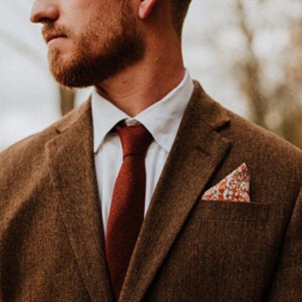 A photo of a man wearing a burnt orange tie and a an orange floral pocket square