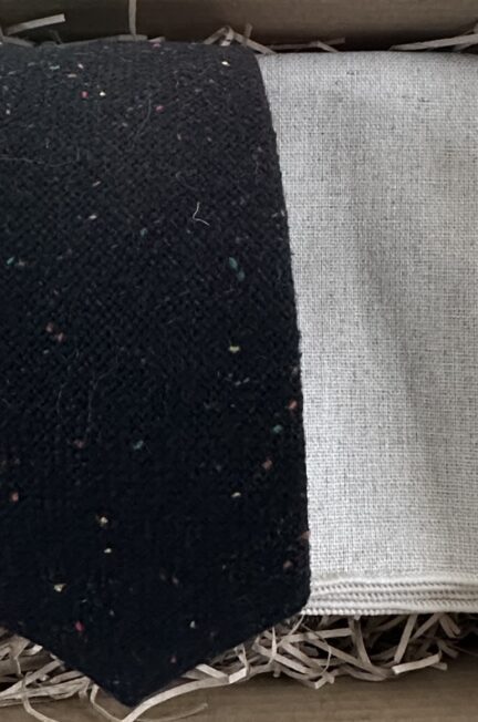 A photo of a black, flecked wool tie and a cream linen pocket square