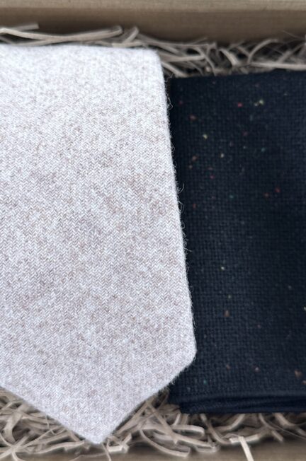 A photo of a men's cream wool tie and a black flecked, wool pocket square
