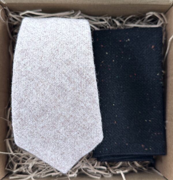 A photo of a men's cream wool tie and a black flecked, wool pocket square