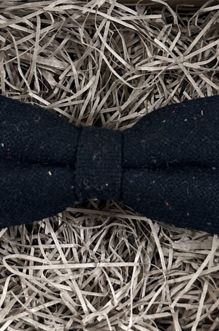 A photo of a black flecked wool bow tie with hints of red, green and yellow woven into the wool