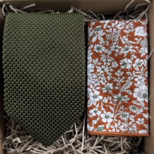 A photo of. a green knitted tie and an orange floral pocket square