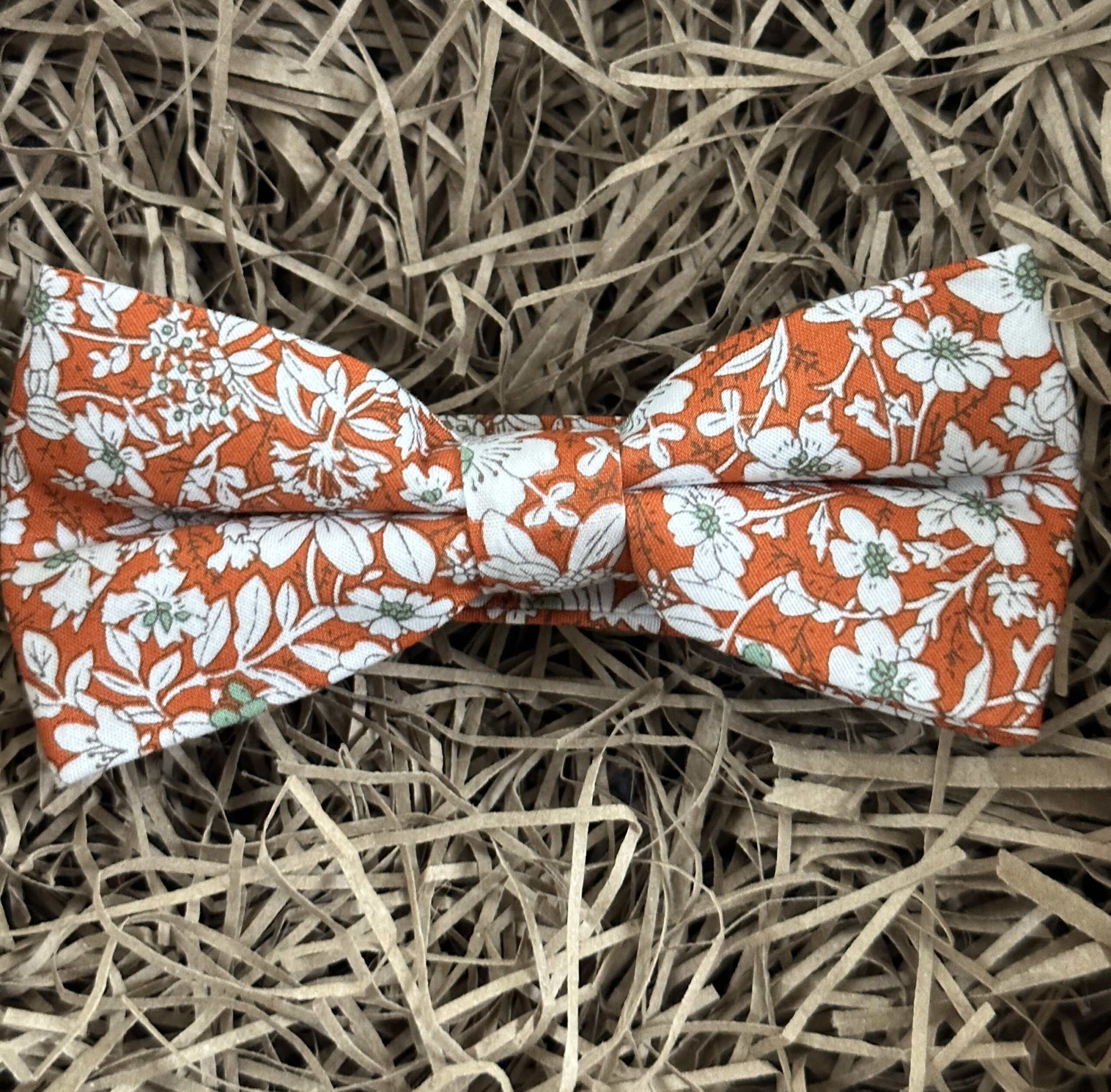 A photo of an orange floral bow tie in cotton. The bow tie is pre-tied and ideal for orange themed weddings.