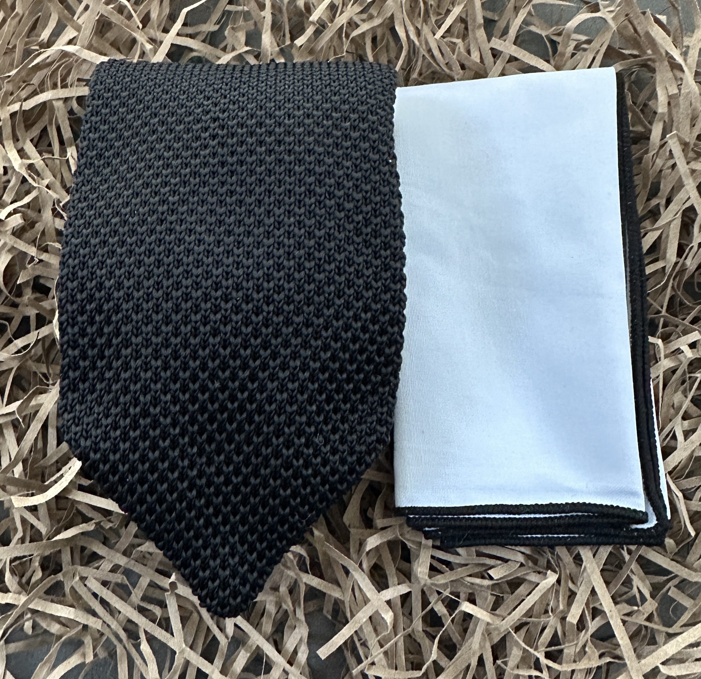 A fabulous men's knitted tie in black with a crisp white handkerchief with a black trim.