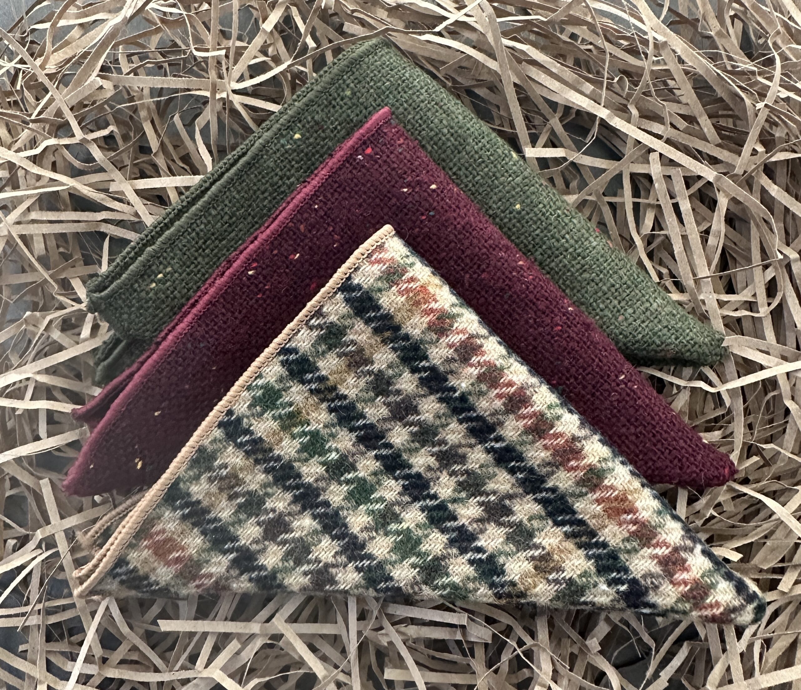 A set of three woolen pocke handkerchiefs for mens and grooomsmen gifts. THe handkerchiefs are in a red and green flecked fabric and a check pattern